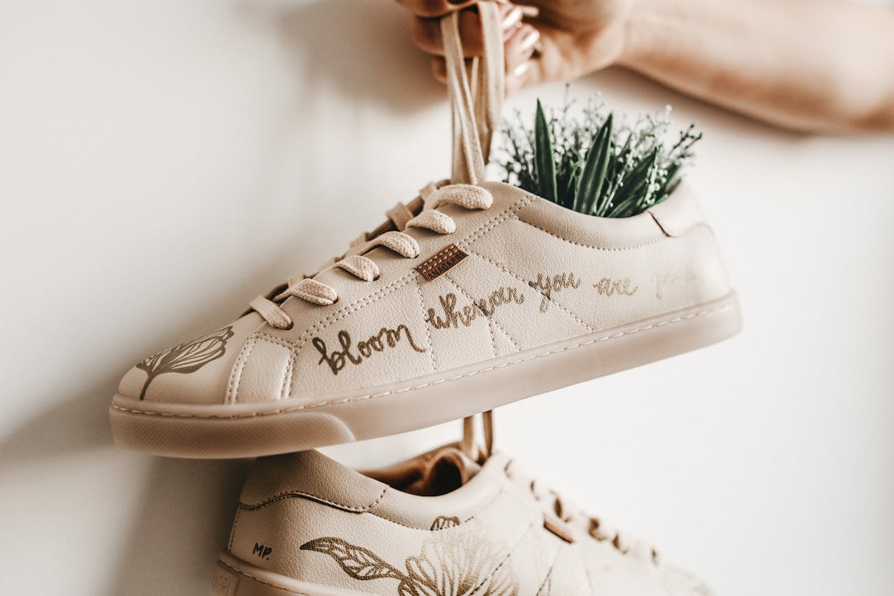 home-hero Close-up of beige sneakers with plant design and 'bloom where you are planted' script.