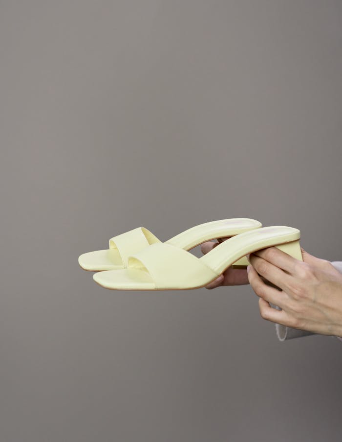 services-cta Stylish yellow heels presented on a neutral grey background held by a pair of hands in a studio setting.